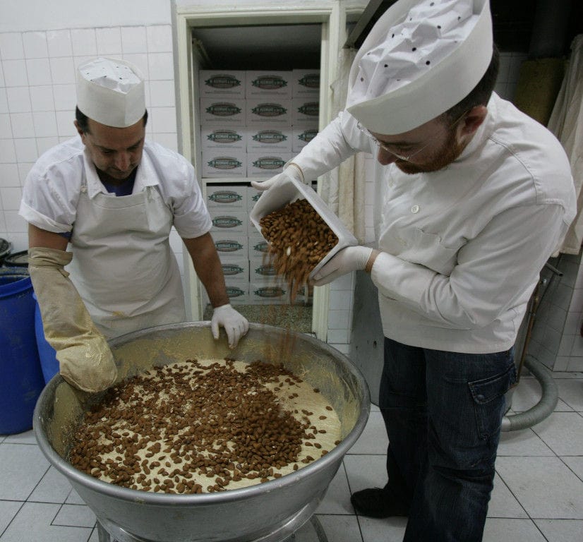 man οverturning almonds in a basin with white composition at 'M. Kosmidis' workshop and another man watching